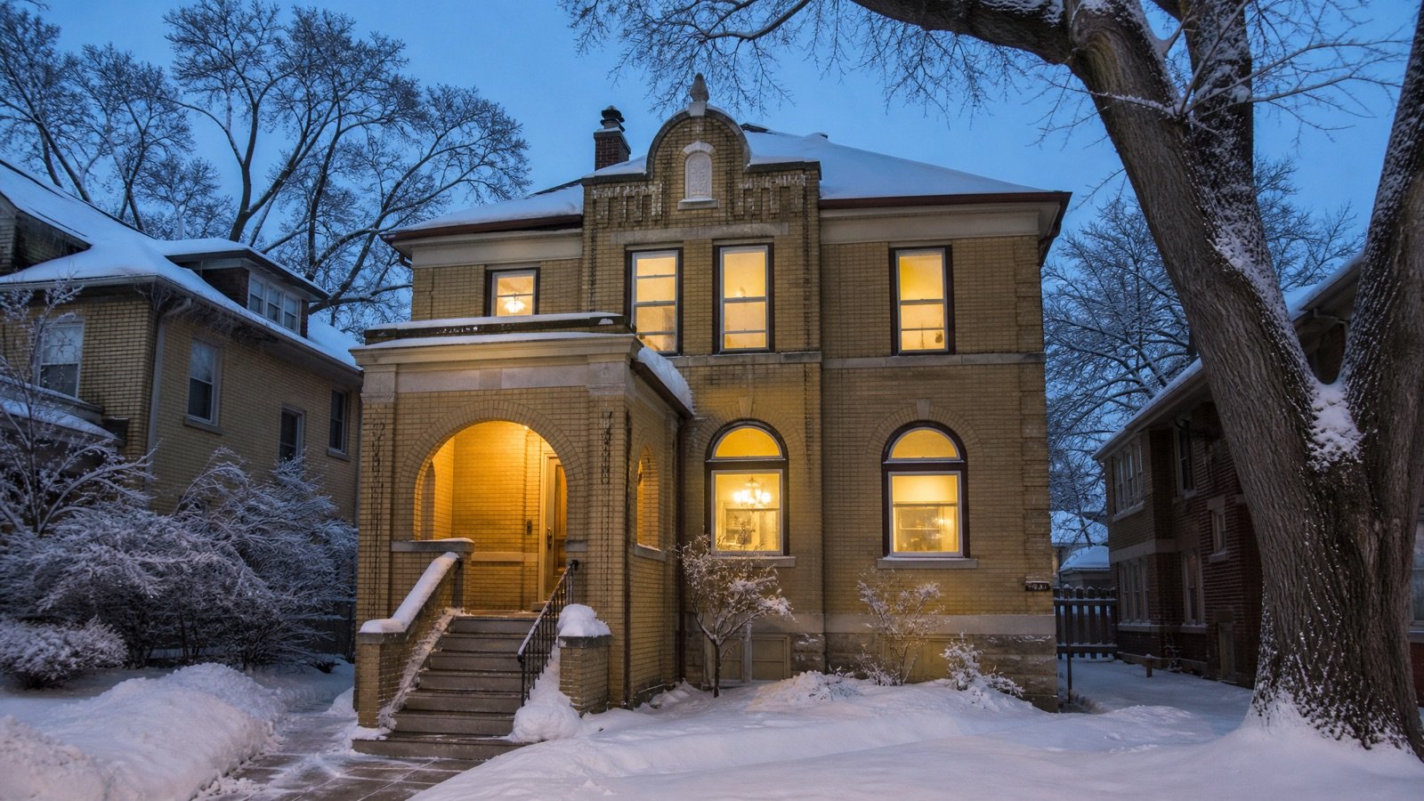 A snow-covered brick house on a quiet Milwaukee street at dusk